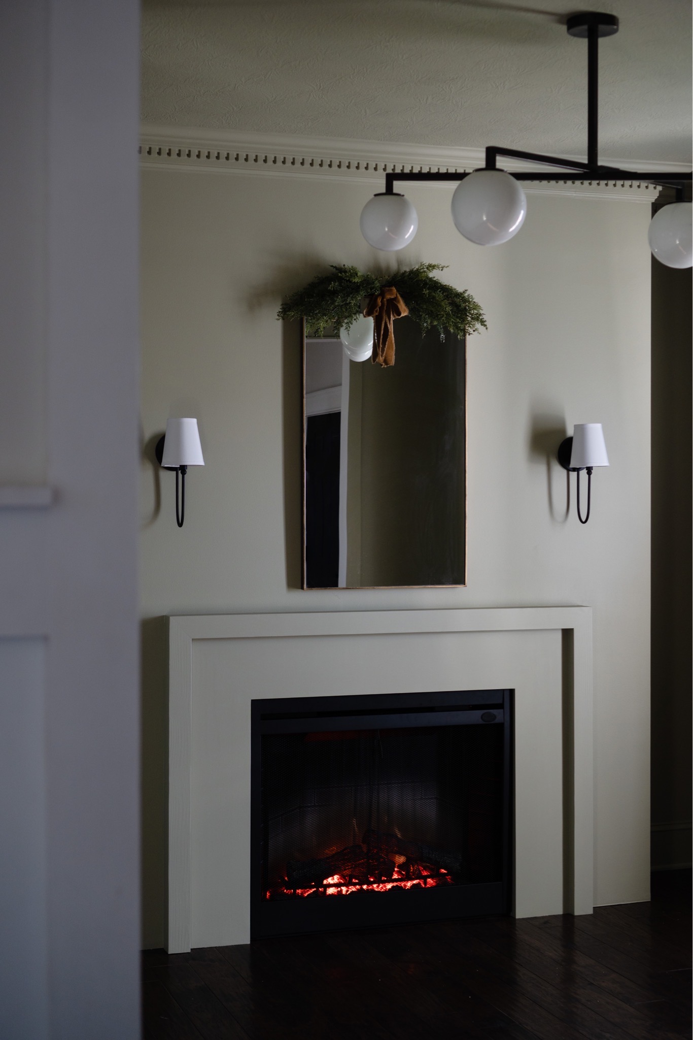 Christmas greenery and ribbon hang on a brass rectangular mirror above a new modern fireplace. 